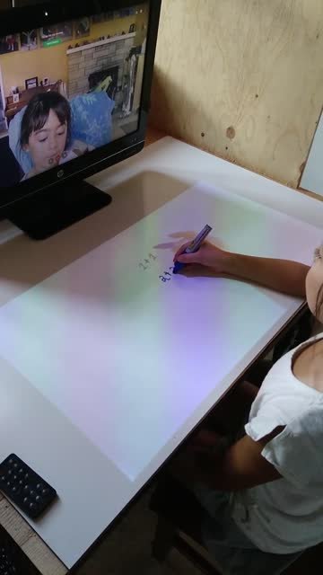 Student writing on an illuminated APPEAR tabletop while meeting remotely